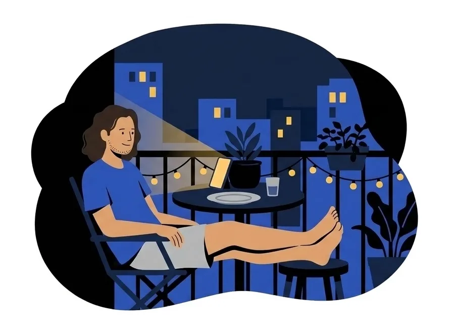 Luca in a folding chair on a balcony at night with his feet on a stool, a phone propped against a plant pot on the table, string lights behind him