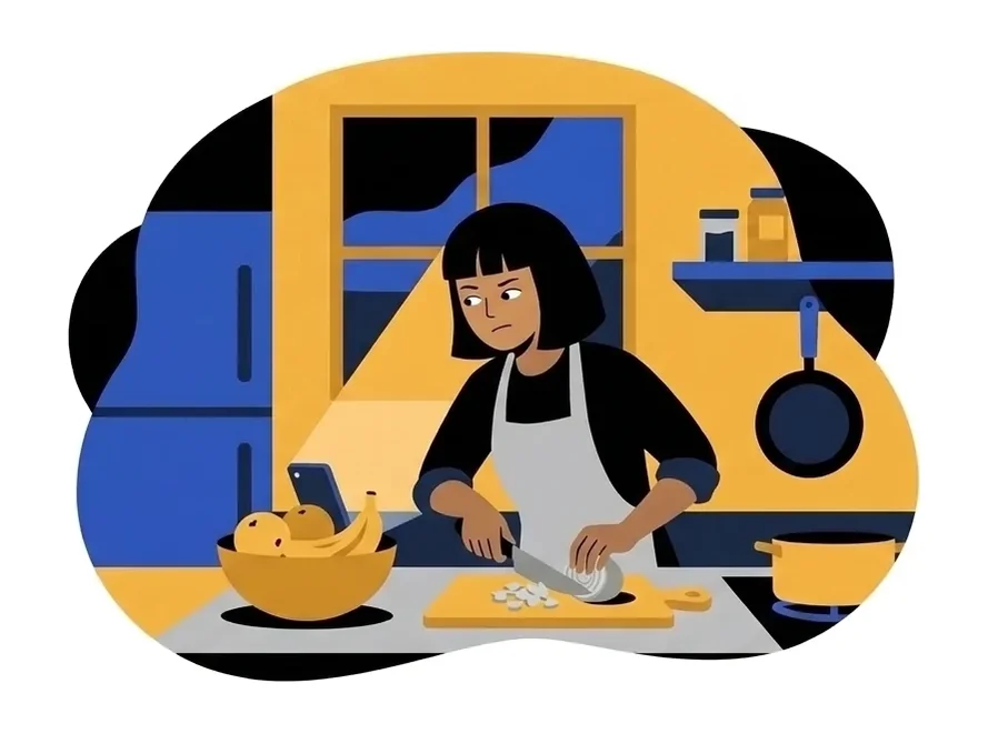 Leila chopping onions at the counter with her eyes turned toward the phone leaning on the fruit bowl